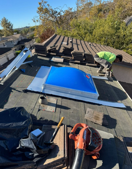 Roofer installing a blue skylight on a flat roof with tools and debris nearby