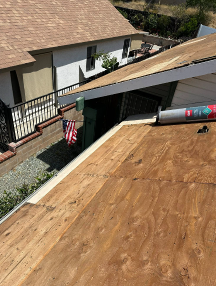 Roof with plywood sheathing and roofing materials beside a house, viewed from above