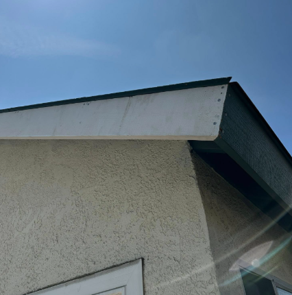 Close-up of a house roof and stucco wall against a blue sky, with sunlight flare