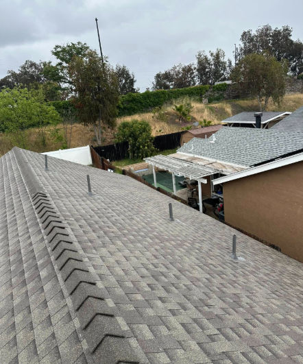 Gray shingled rooftops beside a wooded hillside under an overcast sky