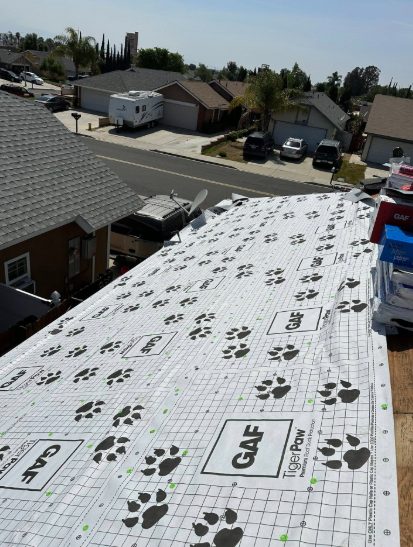 Roof underlayment with grid lines and paw-print markings on a house roof in a suburban neighborhood