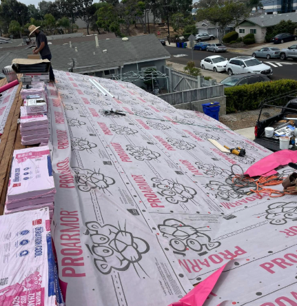 Workers installing pink roofing underlayment on a sloped roof in a suburban neighborhood