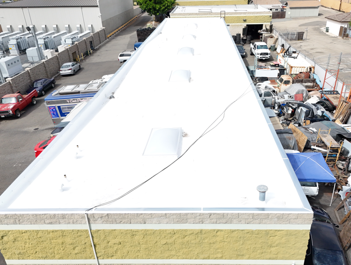 Flat white commercial roof with skylights, next to industrial yard with parked vehicles and equipment