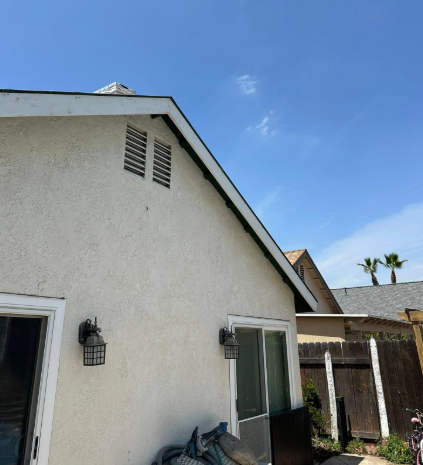 White stucco house exterior with a window, wall lantern, and patio furniture under a blue sky