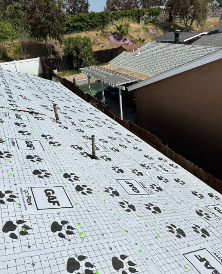Roof underlayment installation with white membrane and black paw-print markings on a house roof.