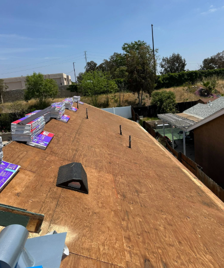 Roof under construction with plywood sheathing, roofing materials, and blue sky above a backyard