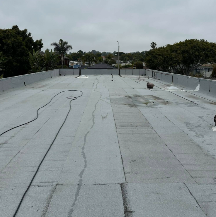 Flat rooftop with white waterproofing membrane and scattered cables under an overcast sky