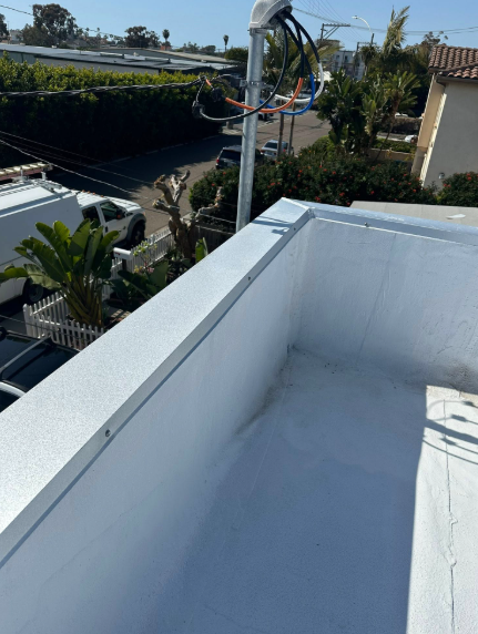 Rooftop terrace with white walls and flooring, overlooking trees and neighboring houses on a sunny day