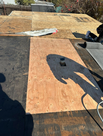 Wooden roof deck under construction with plywood sheets, tools, and shadows in bright sunlight