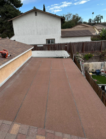 Rooftop covered in brown roofing felt with neighboring houses and a fence in the background