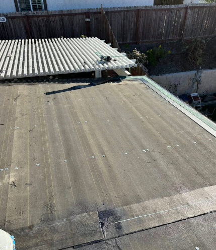 Rooftop with corrugated panels and a fenced backyard in the background.