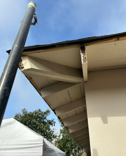 Damaged roof eaves on a beige building with a black pole in the foreground under a blue sky