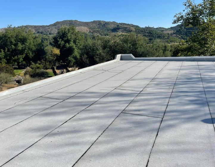 Flat white rooftop with trees and hills under a blue sky