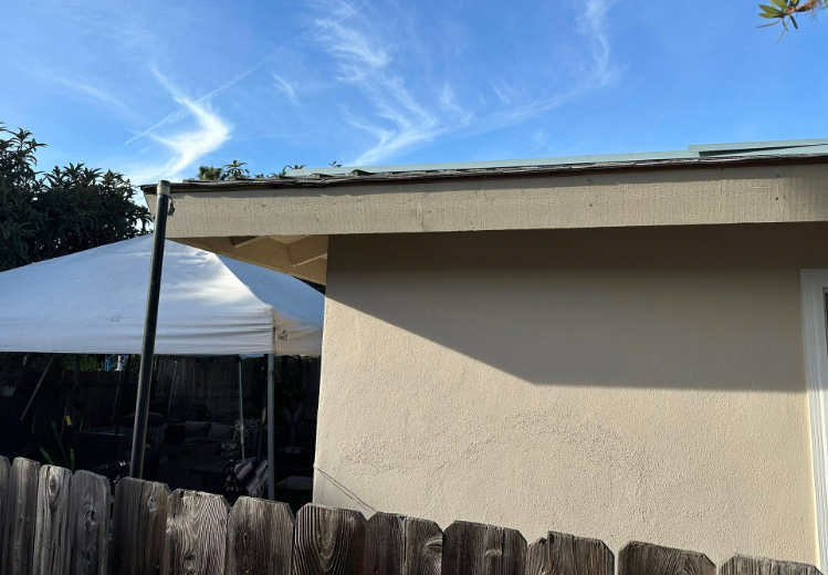Backyard shed roof with white canopy tent and wooden fence under a blue sky