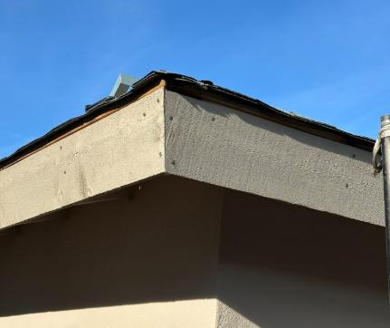 Damaged rooftop corner with peeling stucco under a blue sky