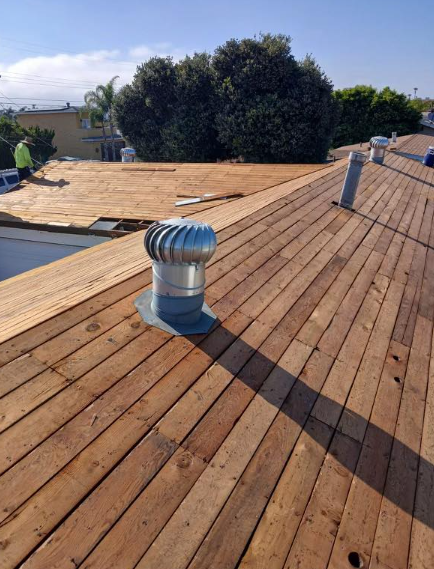 Rooftop with wood decking and a silver roof vent under a clear blue sky