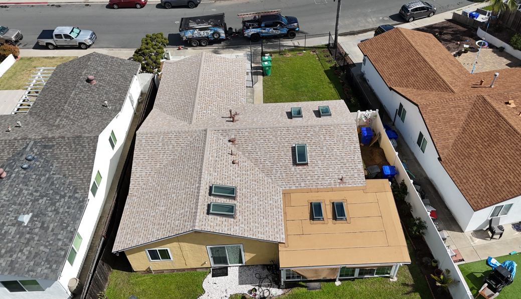 Aerial view of suburban houses with tan roofs, a backyard, and parked cars along the street