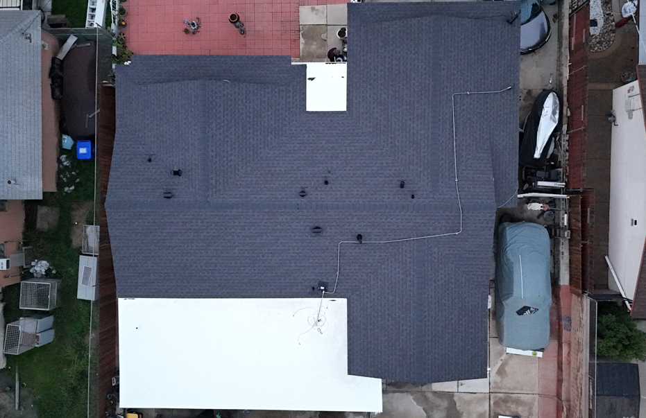Aerial view of a house with a dark roof, white patio extension, and a parked van beside it.
