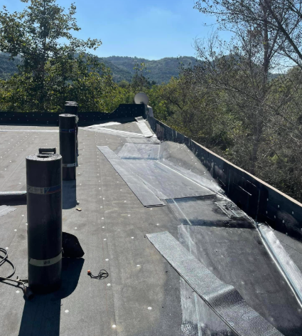 Flat rooftop with vents and protective sheets overlooking trees and distant hills under clear daylight
