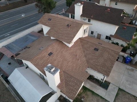 Aerial view of a tan-roofed house next to a road and neighboring homes