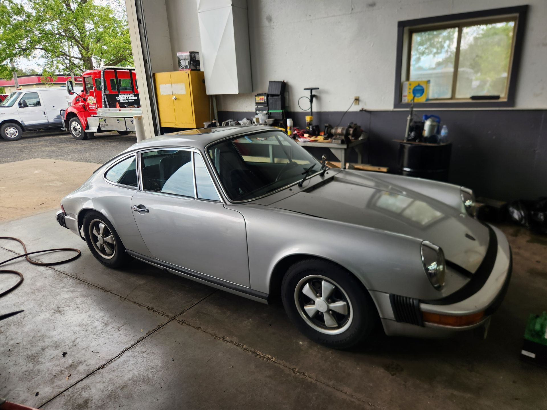 Silver classic Porsche parked in a garage, front-left view with black roof and polished body.