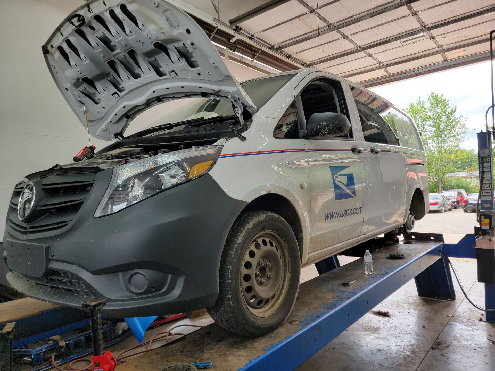 Gray car on a lift in a repair shop, hood open for maintenance