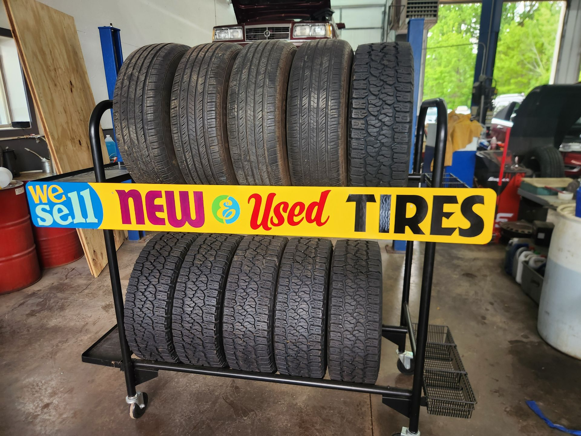 Tire shop display with stacks of used tires and a bright sign reading “We sell new & used tires”