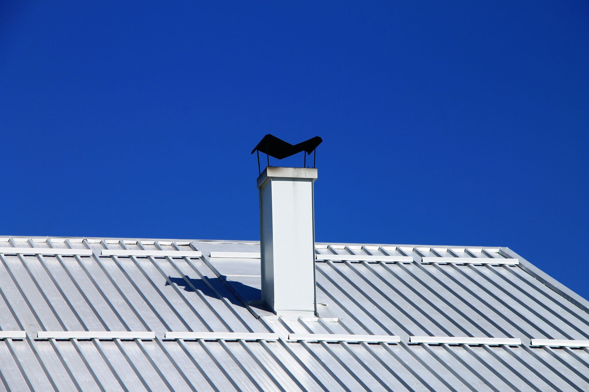 White metal roof with white chimney against a bright blue sky.