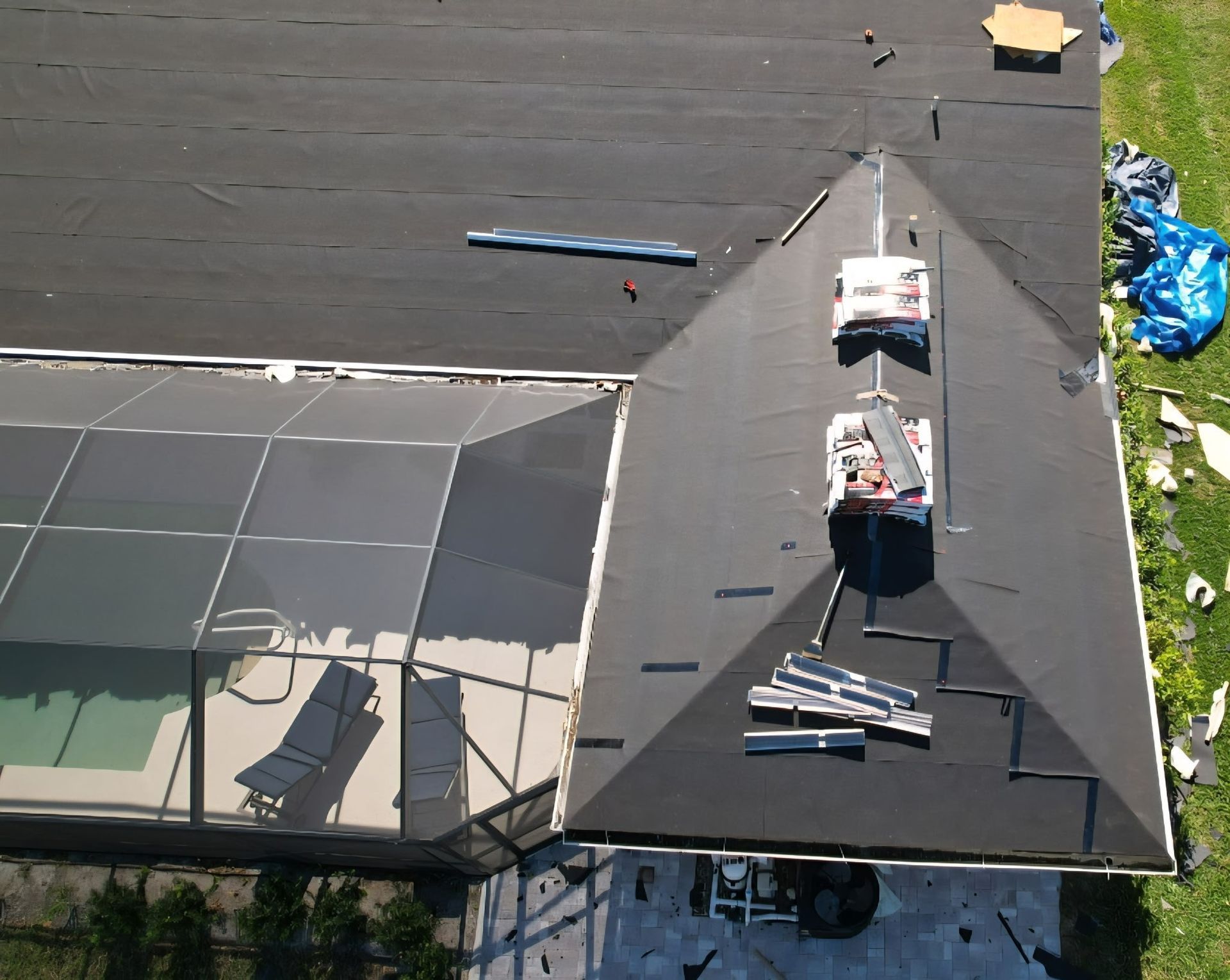 View of a dark roof, partially under construction, with a screened-in pool area to the left.