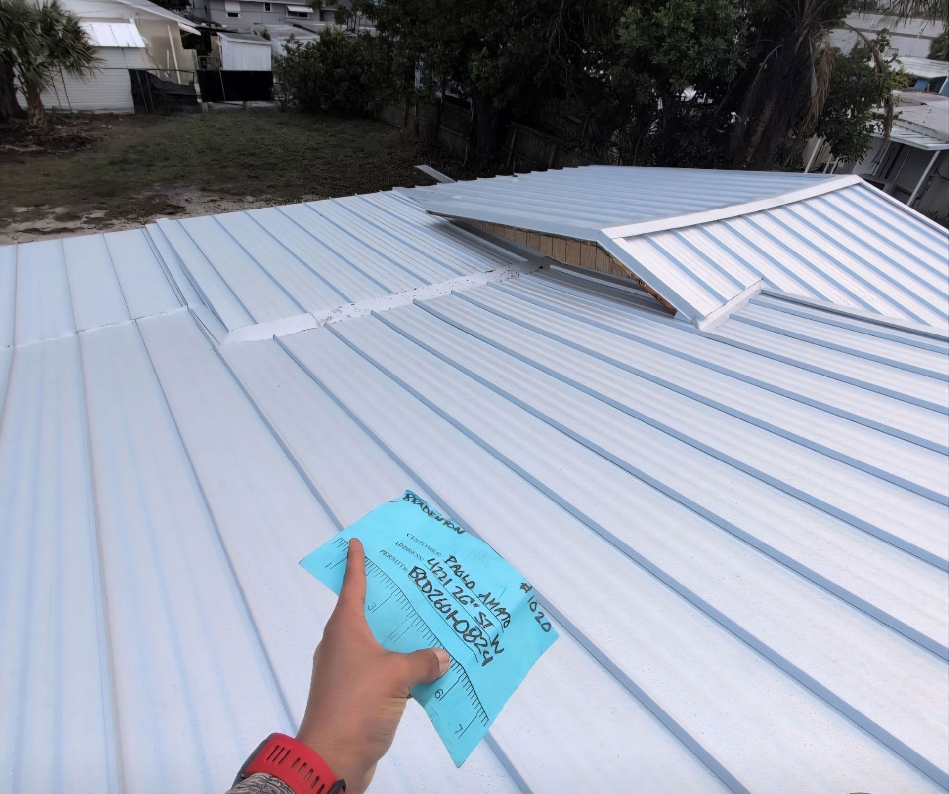 Hand holding a blue note on a shiny, light-blue metal roof, with a skylight.