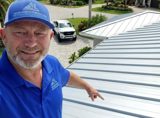 Man in blue shirt and cap points at metal roof; truck in background.