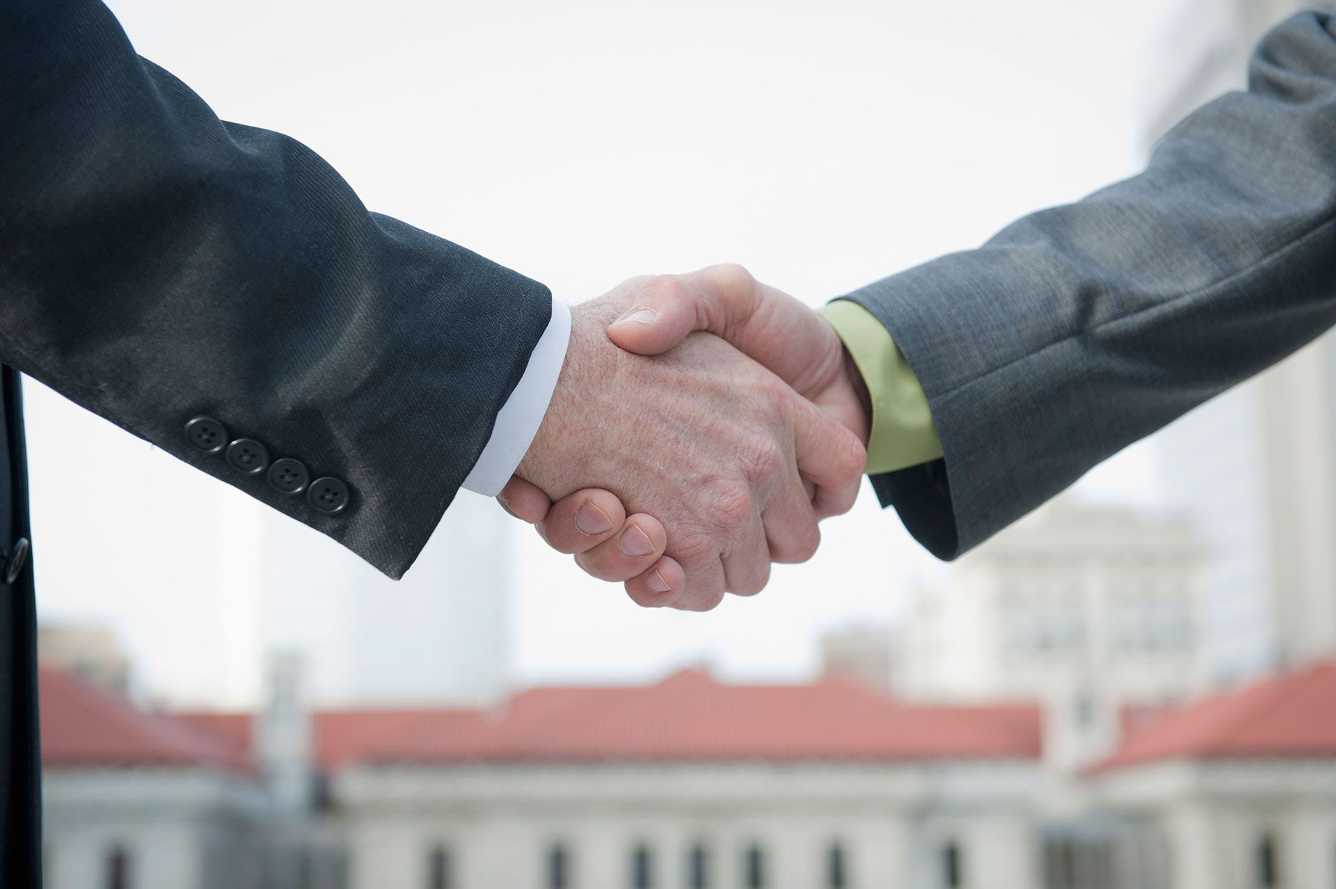 Two businessmen shaking hands, formal attire, cityscape background.