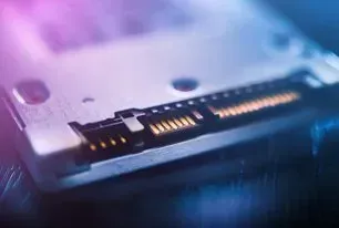 Close-up of a SATA data and power connector on a silver SSD, highlighted by vibrant pink and blue lighting.