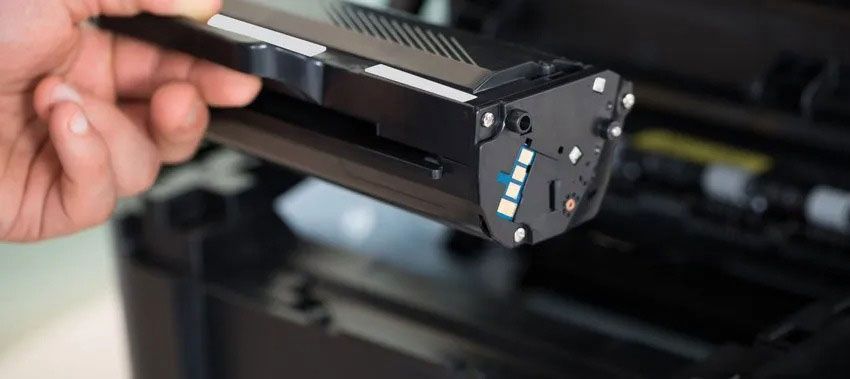 A person holding a black printer toner cartridge, likely installing it in a printer.