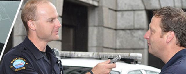 A police officer interviewing a man outside. Both are looking at a small device.