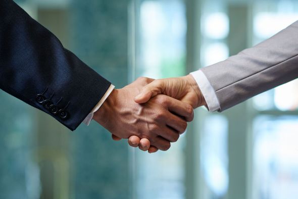 Two people in business suits shaking hands; professional setting.