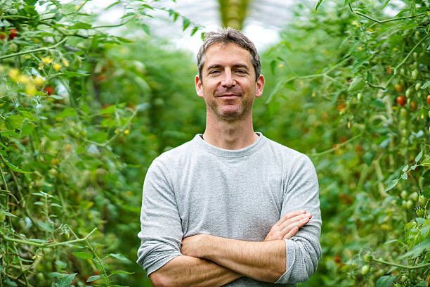 A man is standing in a greenhouse with his arms crossed.