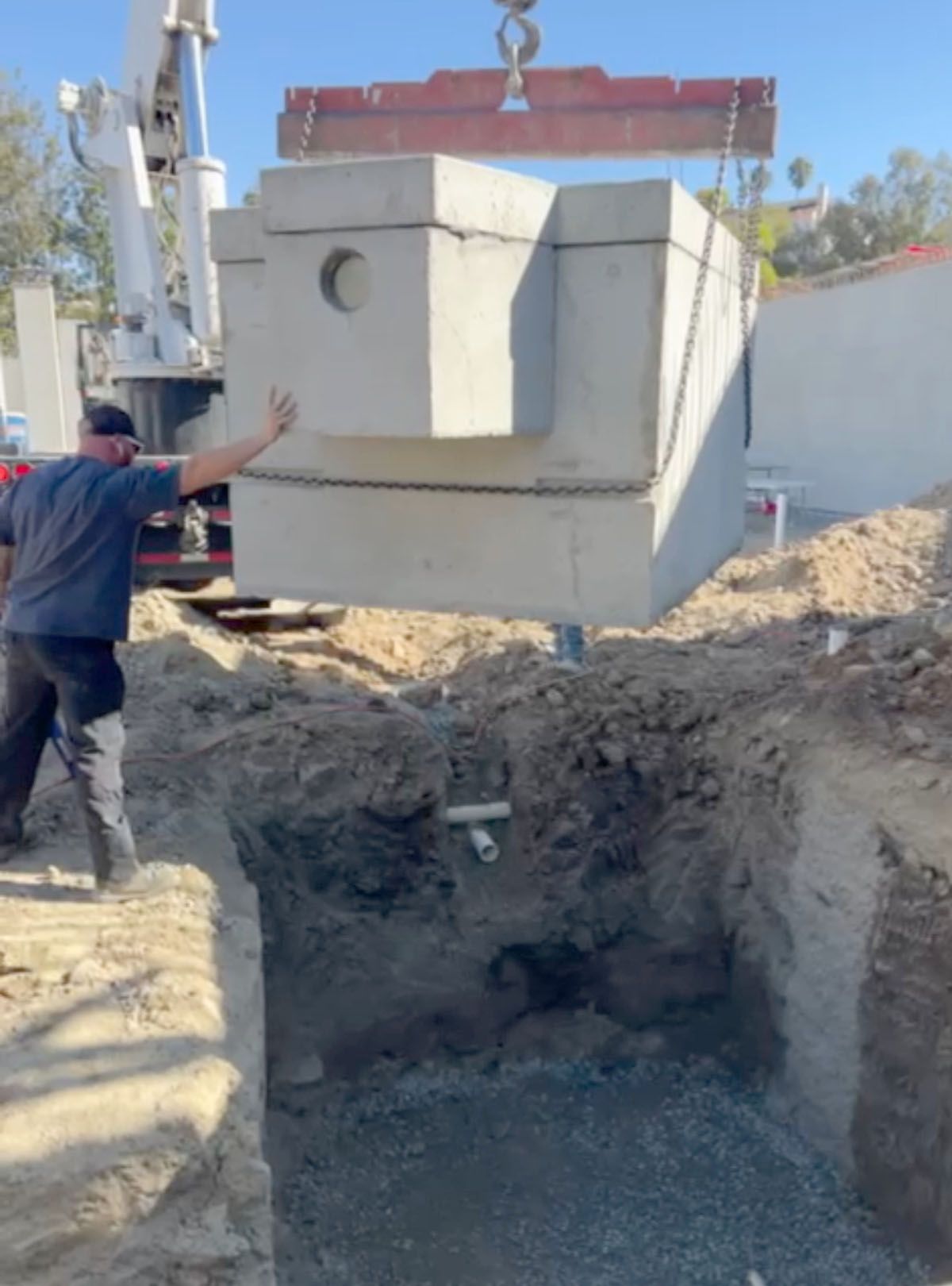 A man is guiding a large septic tank into a hole