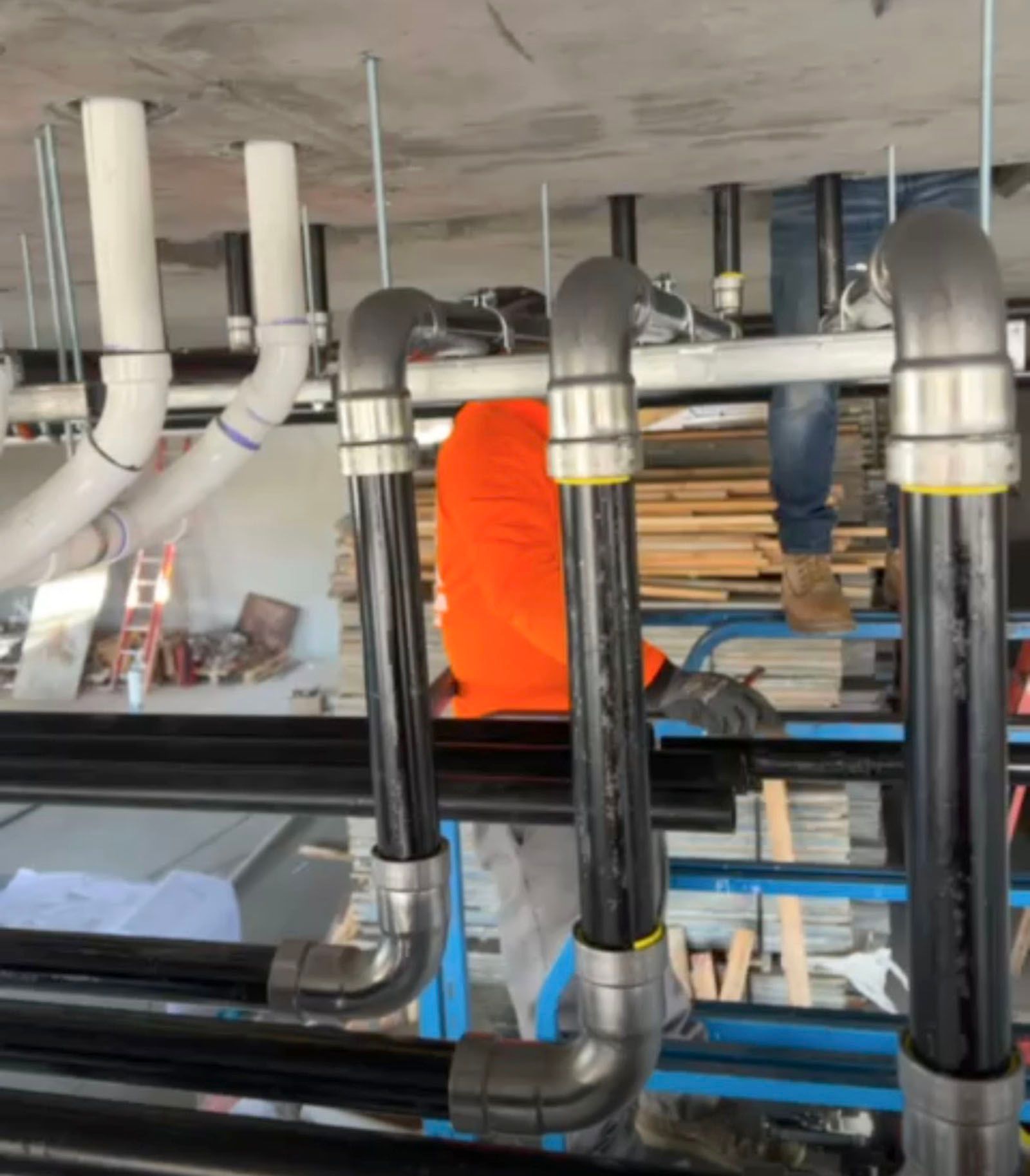 A man in an orange vest is standing next to a row of pipes
