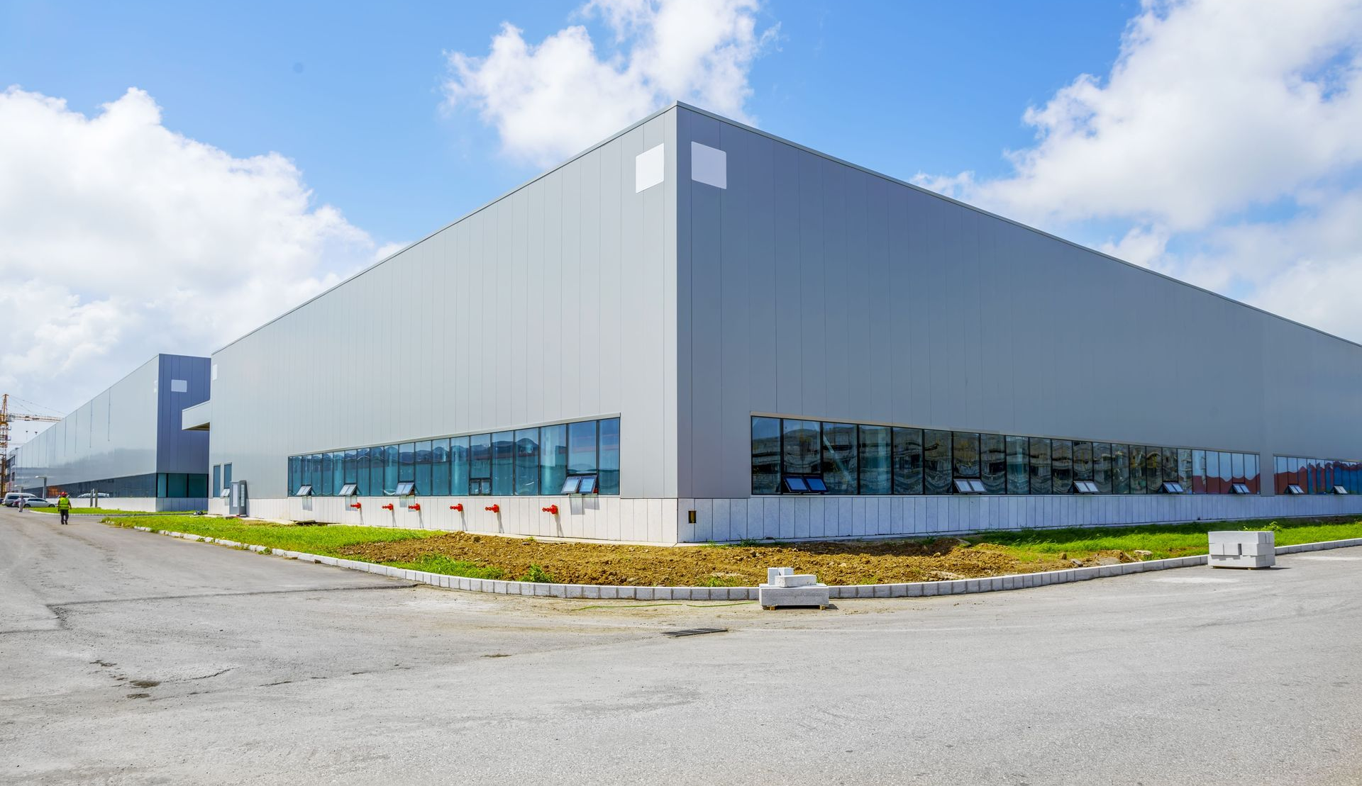 Large gray industrial warehouse with blue windows under a partly cloudy sky