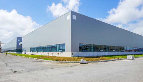 Large gray industrial warehouse with blue windows under a partly cloudy sky