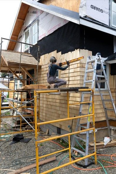 Worker on yellow scaffolding installing bamboo wall panels at a construction site