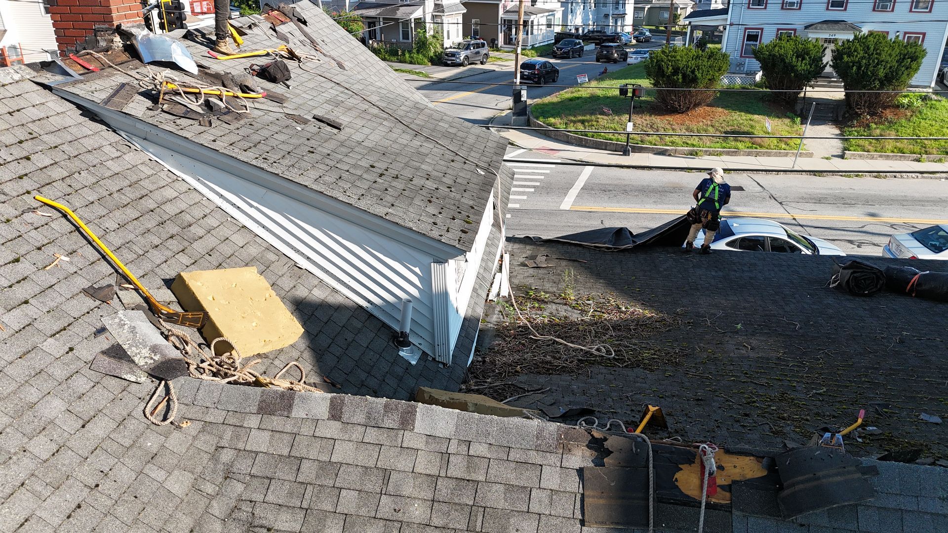 Damaged roof shingles and a torn white roof section overlooking a suburban street and yard