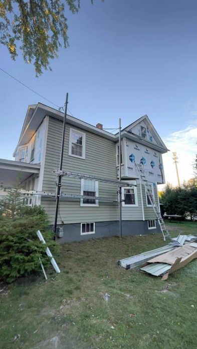 House exterior with scaffolding and construction materials in a grassy yard under a clear sky