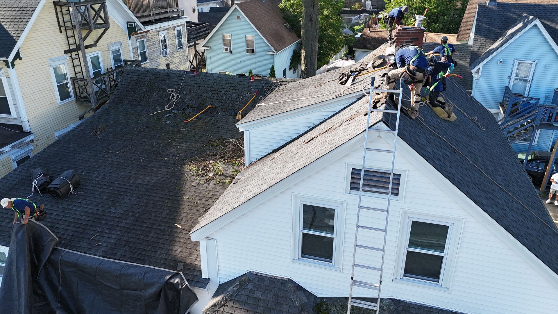 Roofers repairing damaged roofs on houses, with debris and exposed roof sections visible