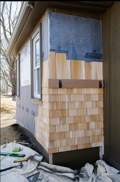 House corner with new wood shingles and blue protective wrap during exterior siding repair