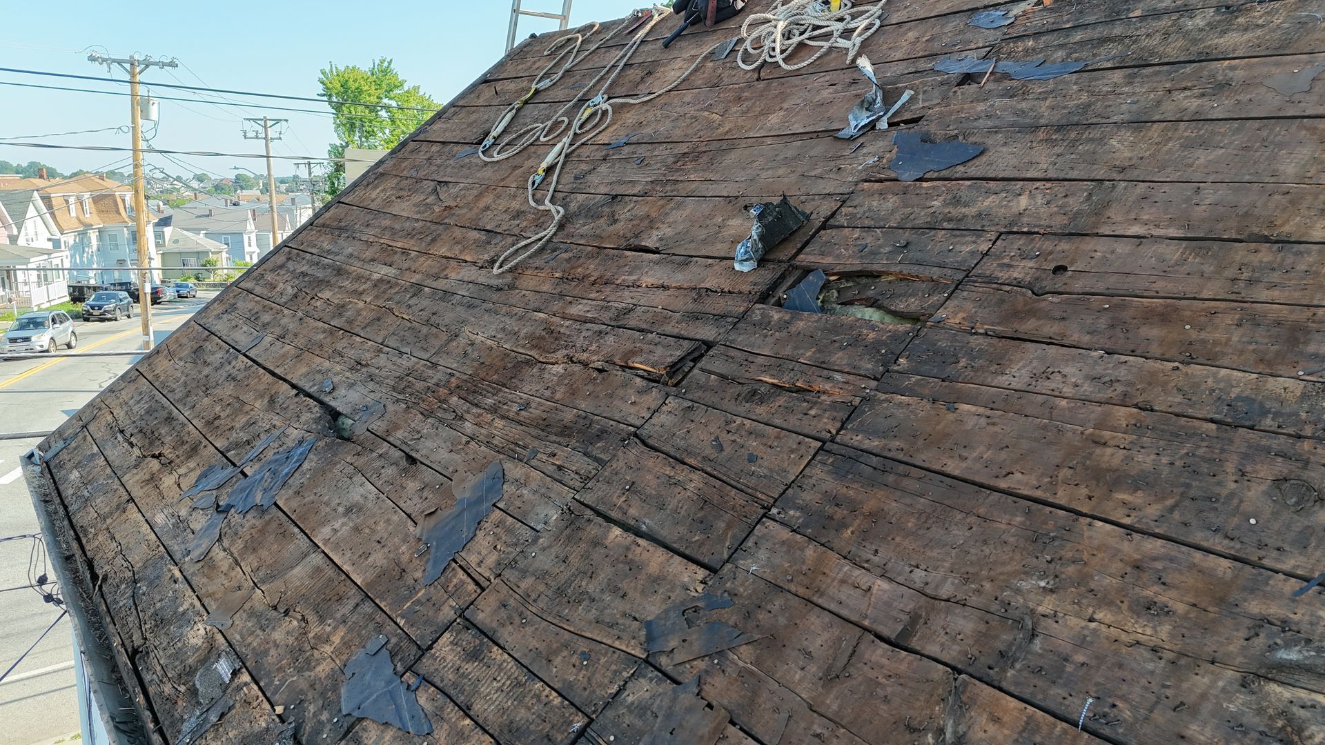 Damaged shingled rooftop with missing tiles and a few loose branches, viewed from above