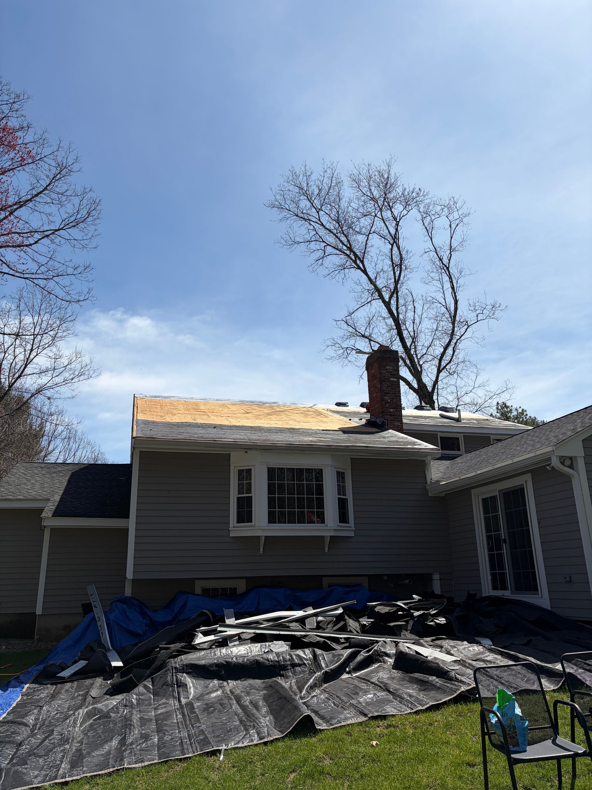 Damaged house roof with tarp and debris after storm, trees visible behind the home