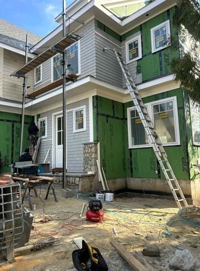House exterior under construction with workers, ladders, scaffolding, and building materials scattered below.