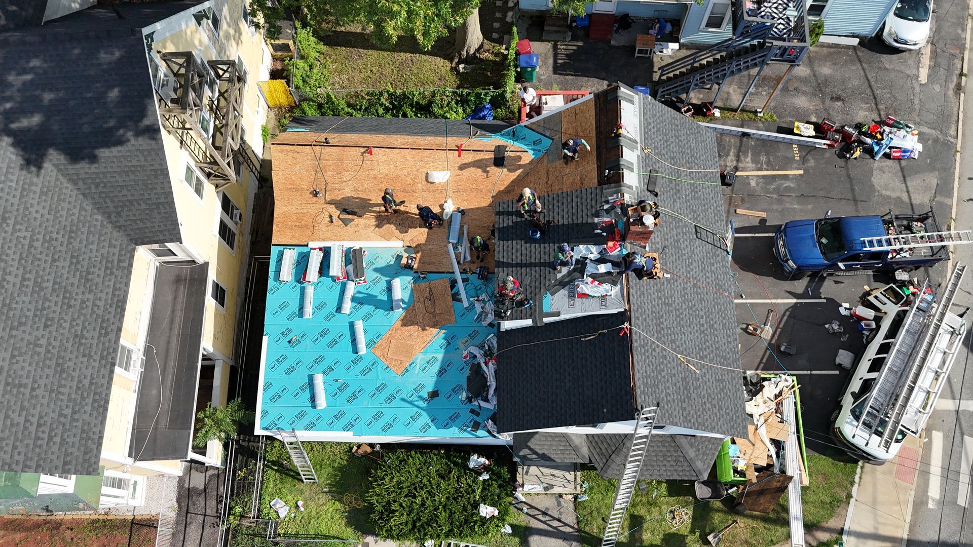 Aerial view of roof repair with workers, blue tarp, and scattered tools on a residential house